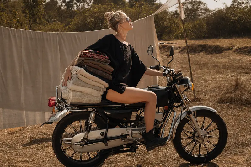 A woman riding a motorcycle with a stack of handwoven shawls